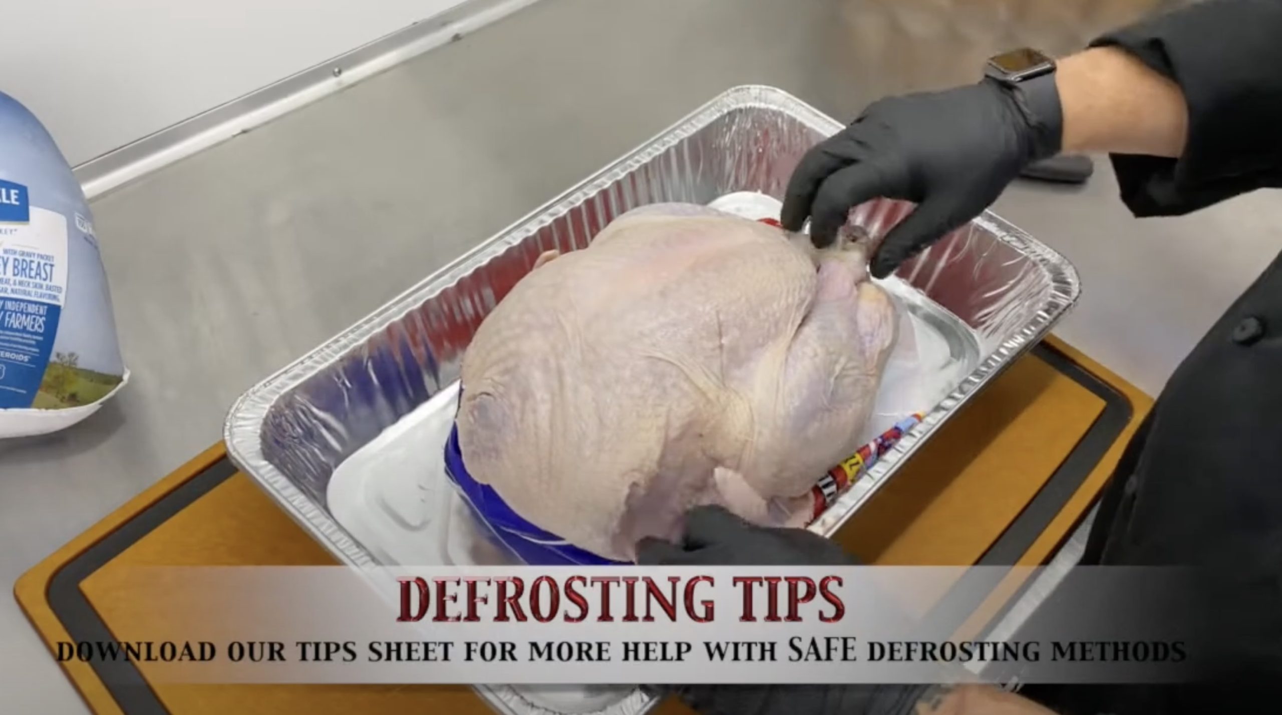 Gloved hand touching a raw turkey in pan.