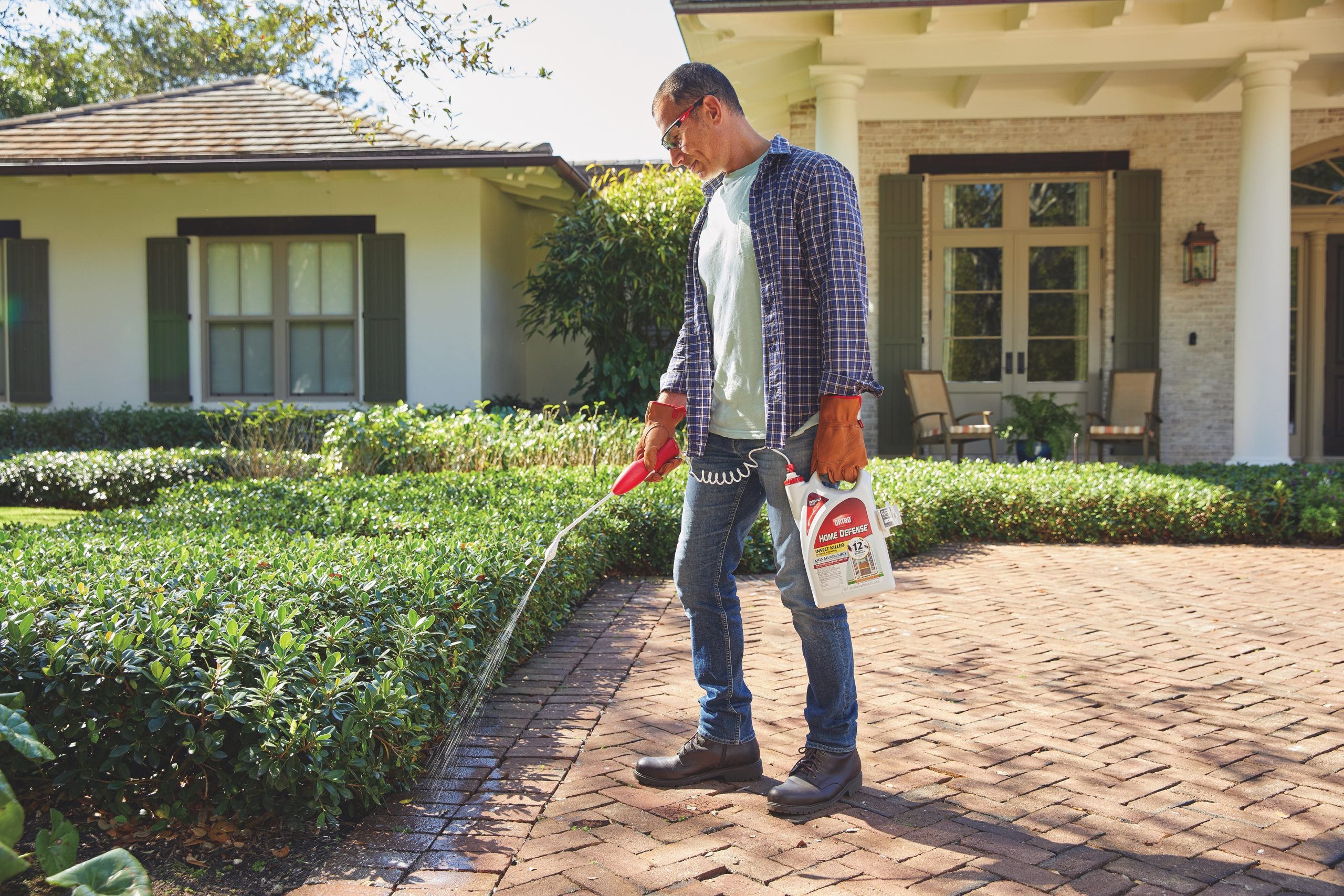 Man sprays insect killer along edge of driveway.